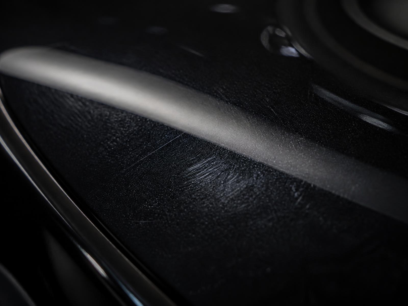 Macro view of black car paint showing fine swirl marks under a light strip
